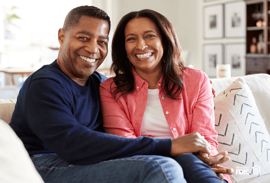 a couple sits on their couch smiling because their Academy Bank IRA is helping them save for retirement