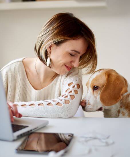a woman smiles at her dog while transferring money using her online banking account