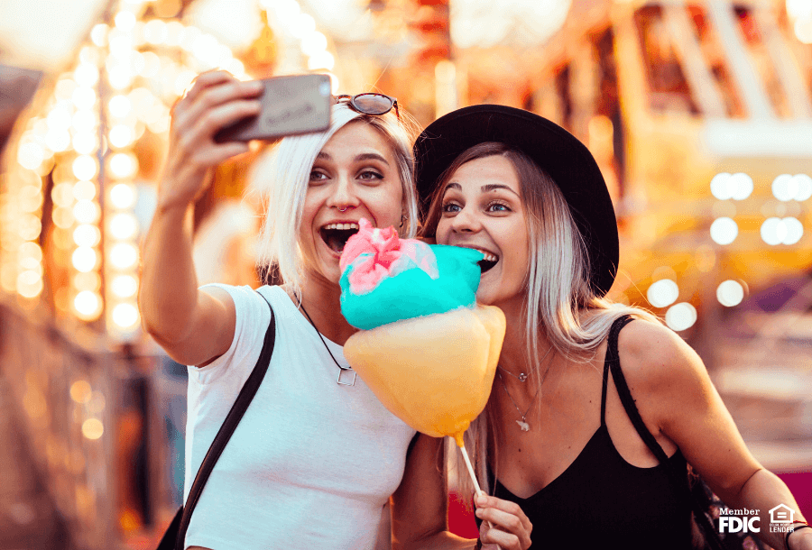 Two women enjoy cotton candy while taking a selfi