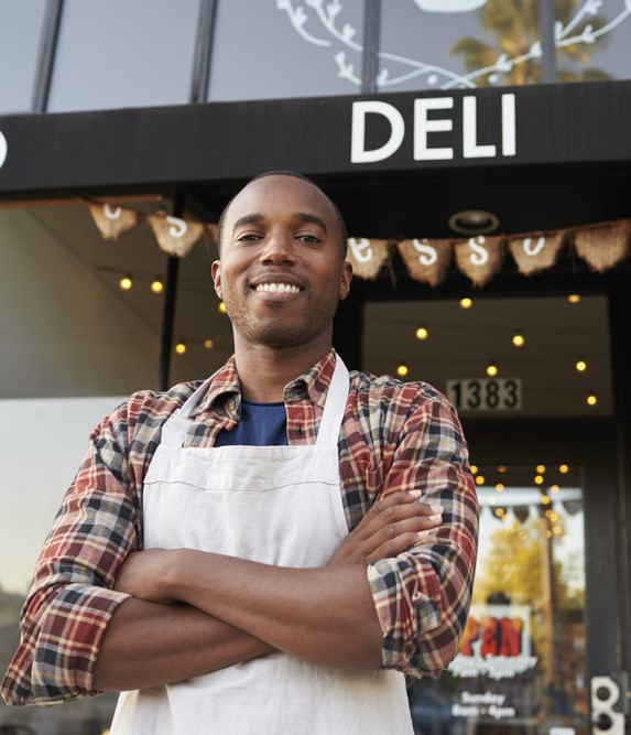 a small business owner stands proudly in front of their deli