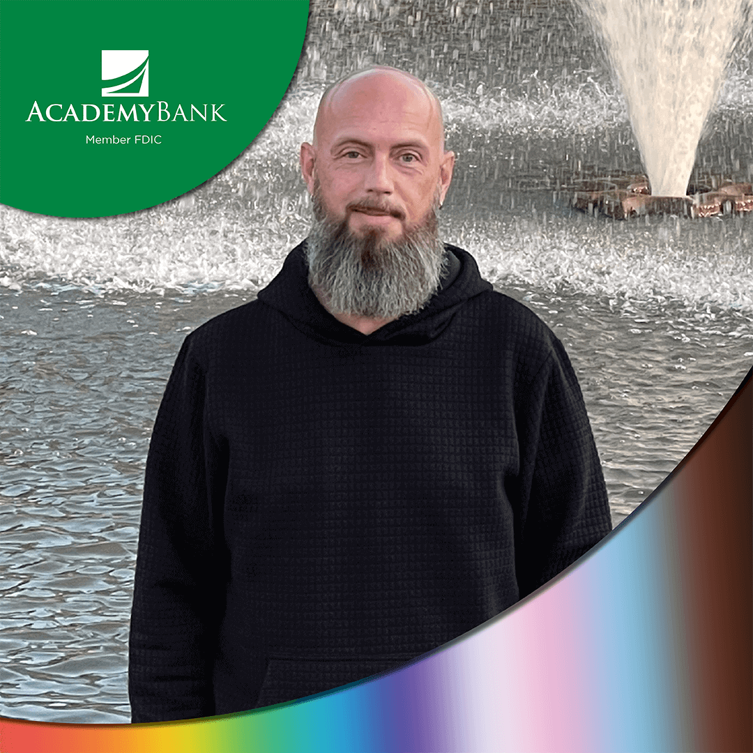 An LGBTQ+ Academy Bank employee poses in front of a fountain. 
