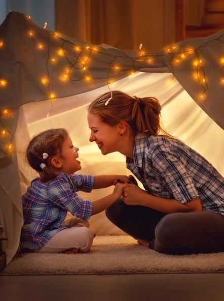a mother and her daughter laugh inside a blanket fort