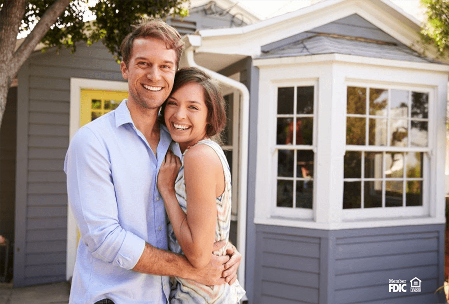 a young couple joyfully stand outside their newly bought home