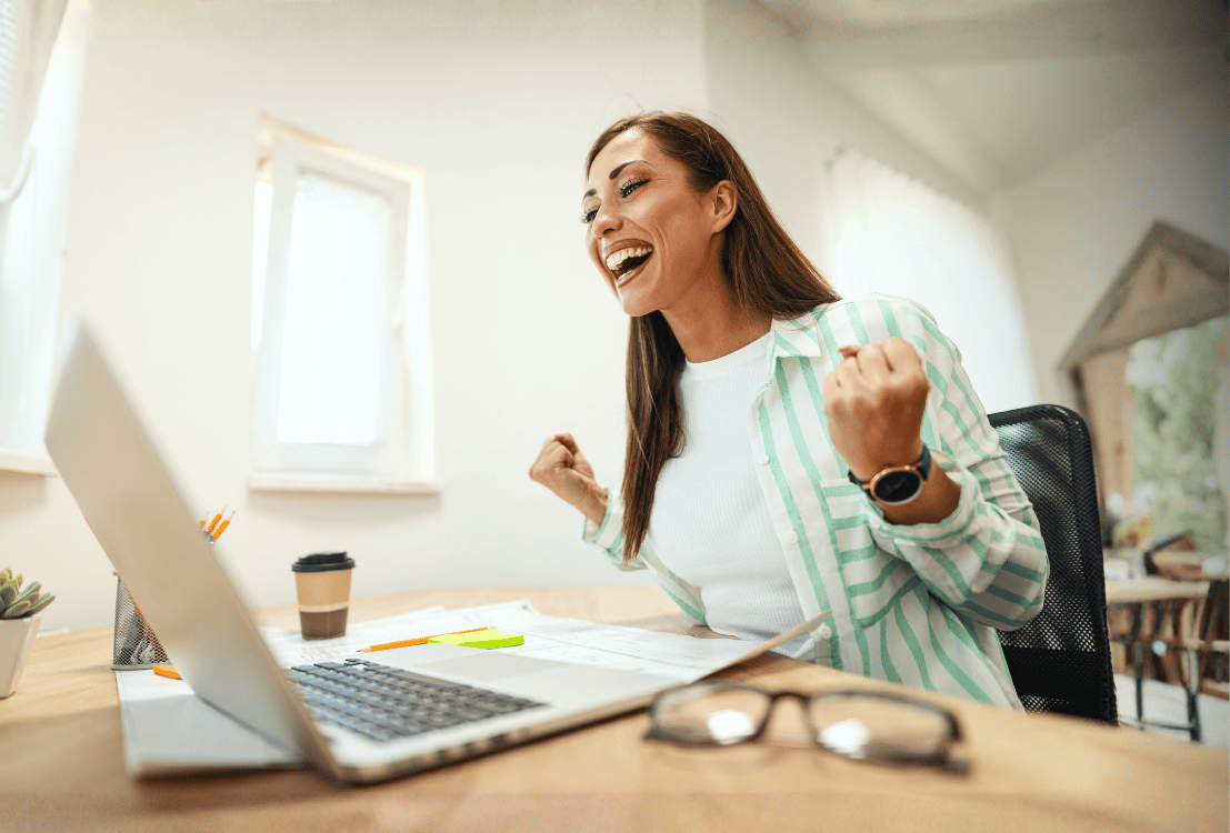 Woman looking at her laptop and celebrating that she has a bank account in good standing.