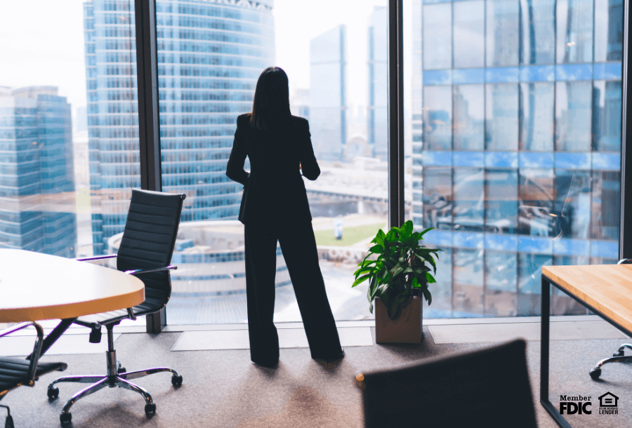 a sole woman stands in an office staring out at the city