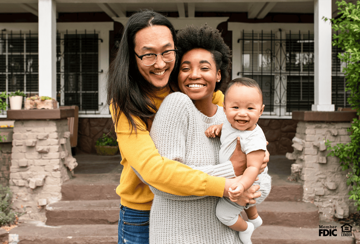Young family smiling in front of their first house, purchased with a FHA home loan.