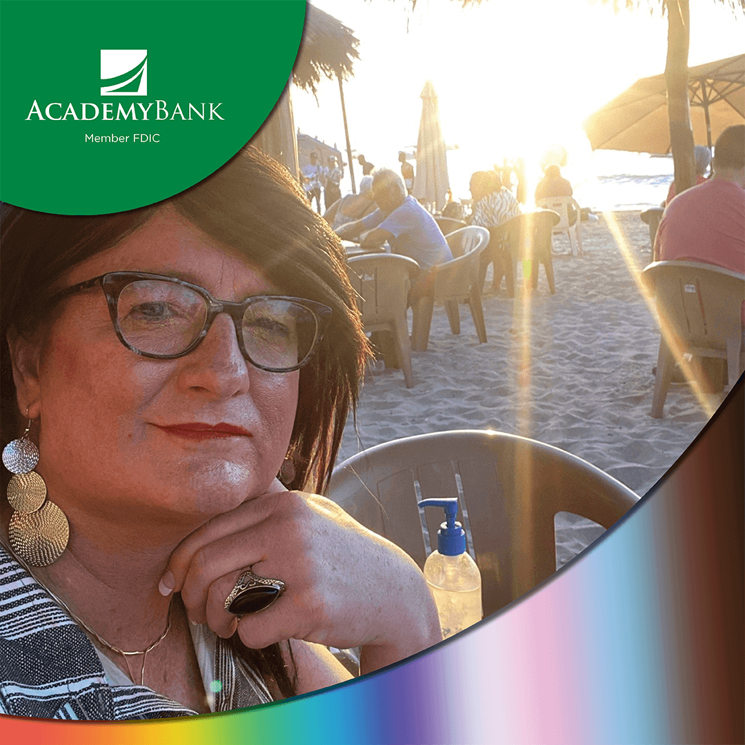 An LGBTQ+ Academy Bank employee sitting on a beach during vacation.
