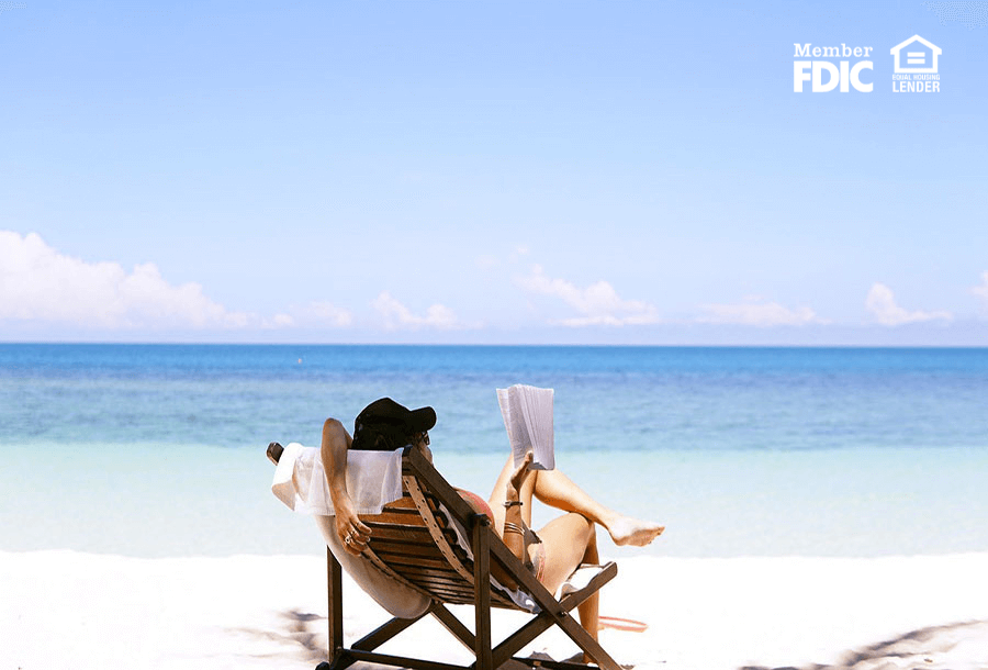 A woman peacefully reading a book in a chair on the beach.