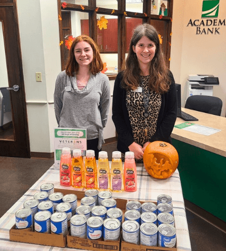 Academy Bank employees pose with donated cans and sanitary products for Days of Giving charity event.