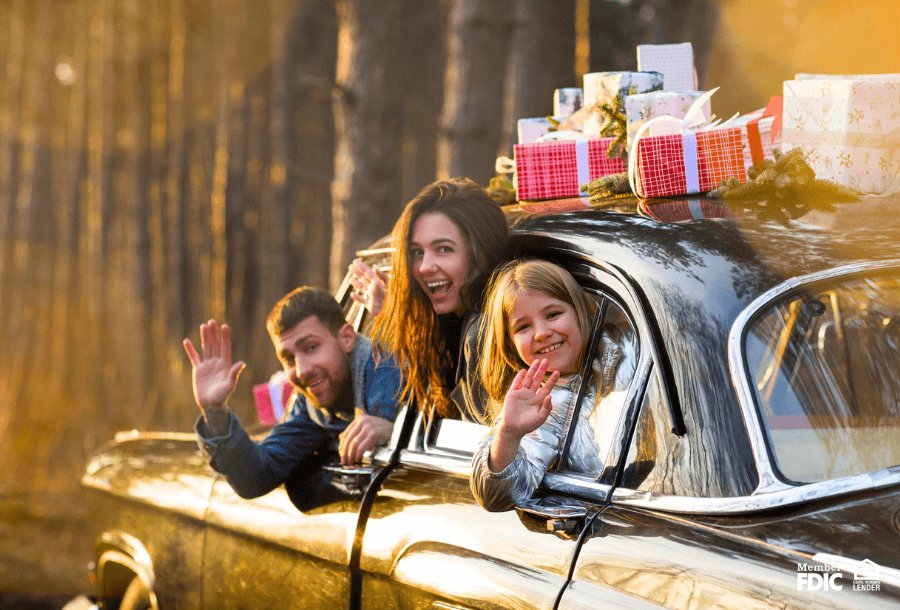A family packs up in a car with gifts on top of it to start their holiday adventure