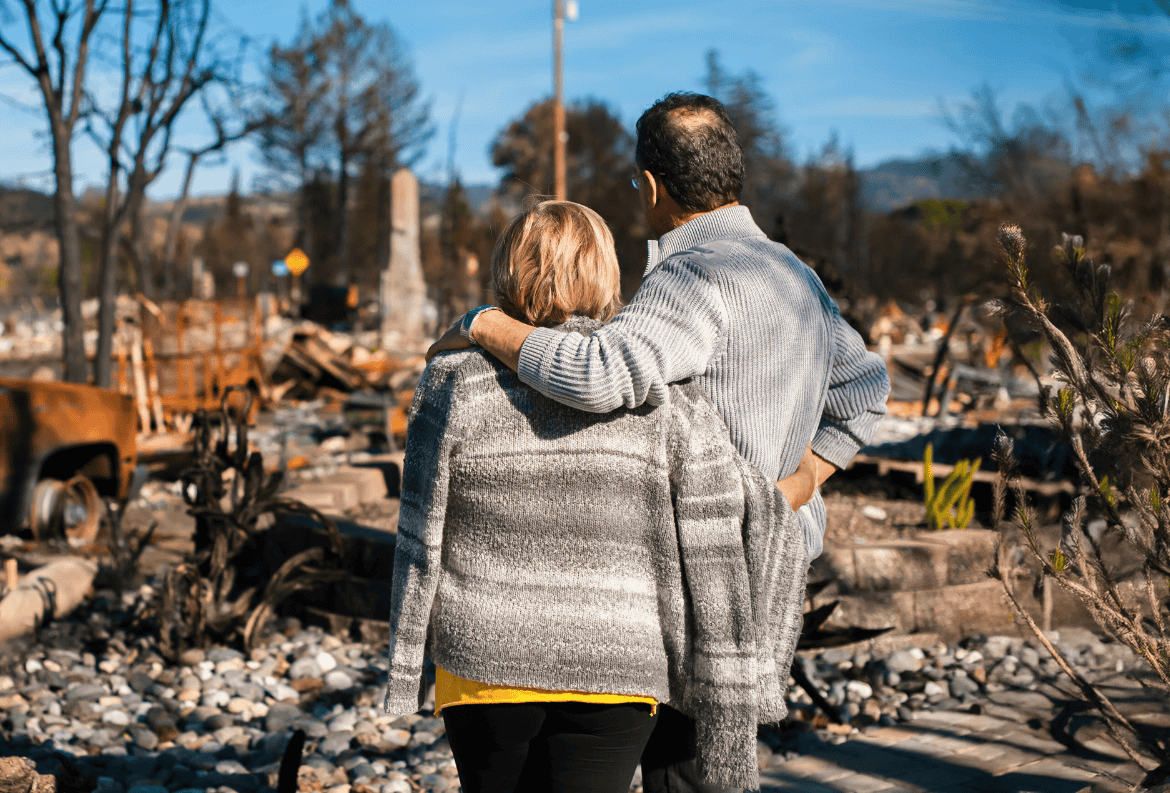 Couple looking at their destroyed property after a disaster and considering using a personal loan to bridge funding gaps.