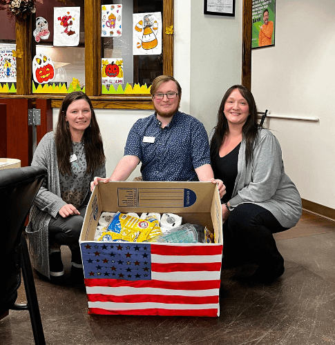 Academy Bank employees show off their box of donated supplies during days of giving charity push