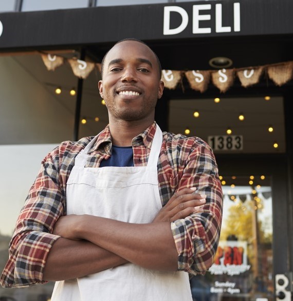 a proud business owner standing outside their deli