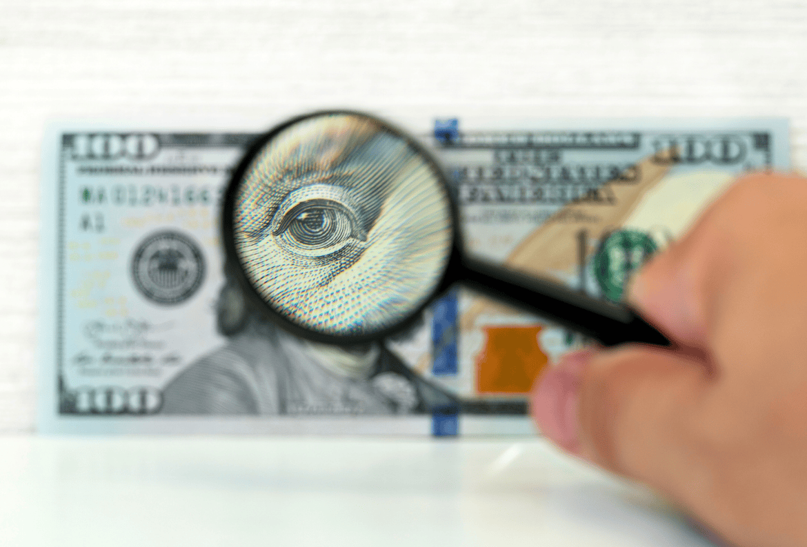 Person reviewing $100 bill for counterfeit