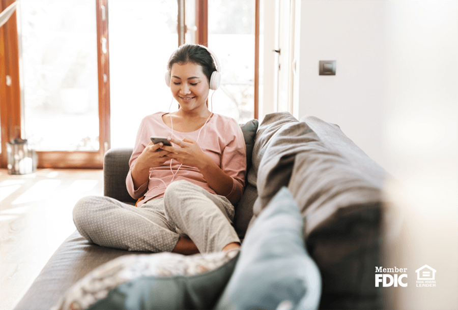 a woman sits on her couch listening to music on her phone